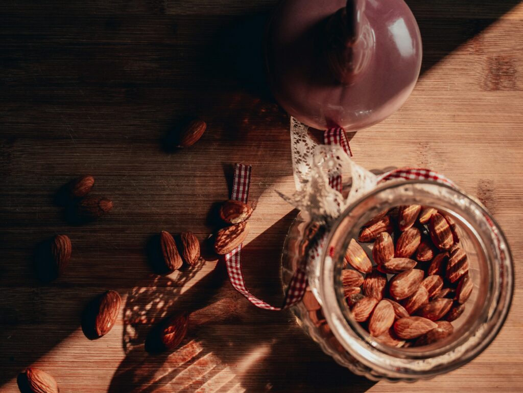 Rustic photo of almonds in a jar with warm lighting and shadows on a wooden table.